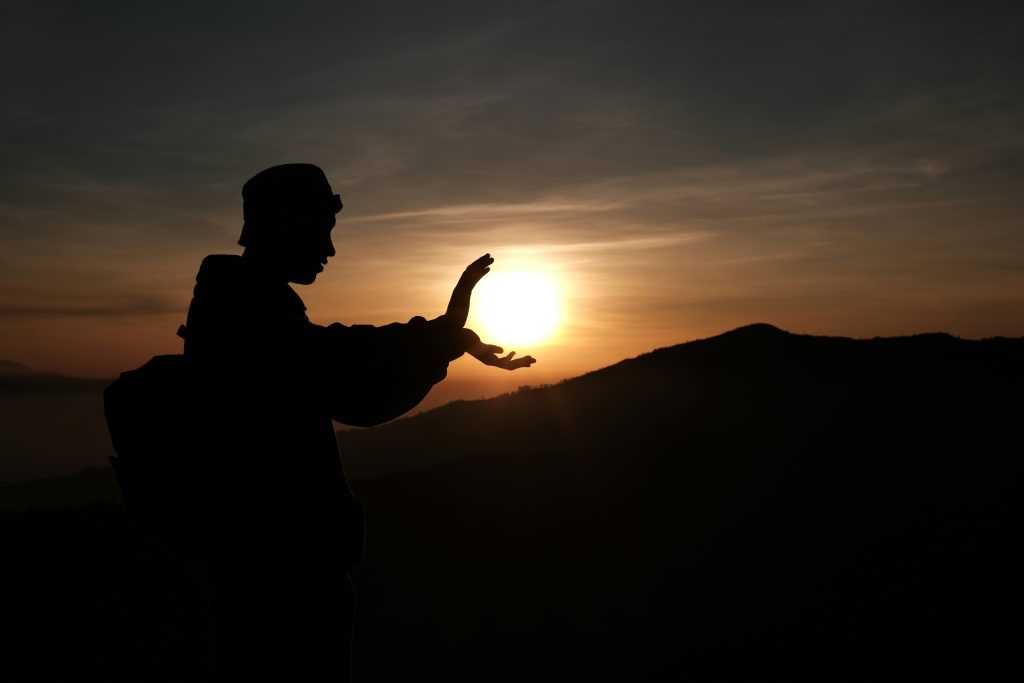 personne semblant tenir un couché de soleil entre ses mains